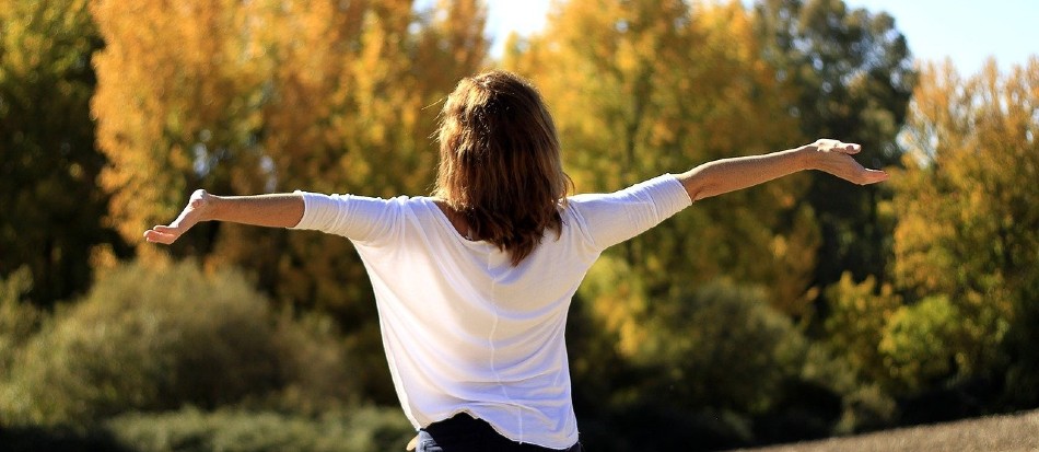 Woman with back facing camera has arms stretched out embracing the sunshine